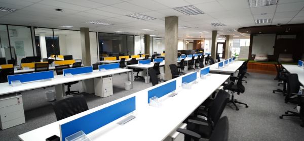 Salão de estações de trabalho do Foccus Workplace, com bancadas brancas, divisórias azuis e cadeiras ergonômicas enfileiradas.
